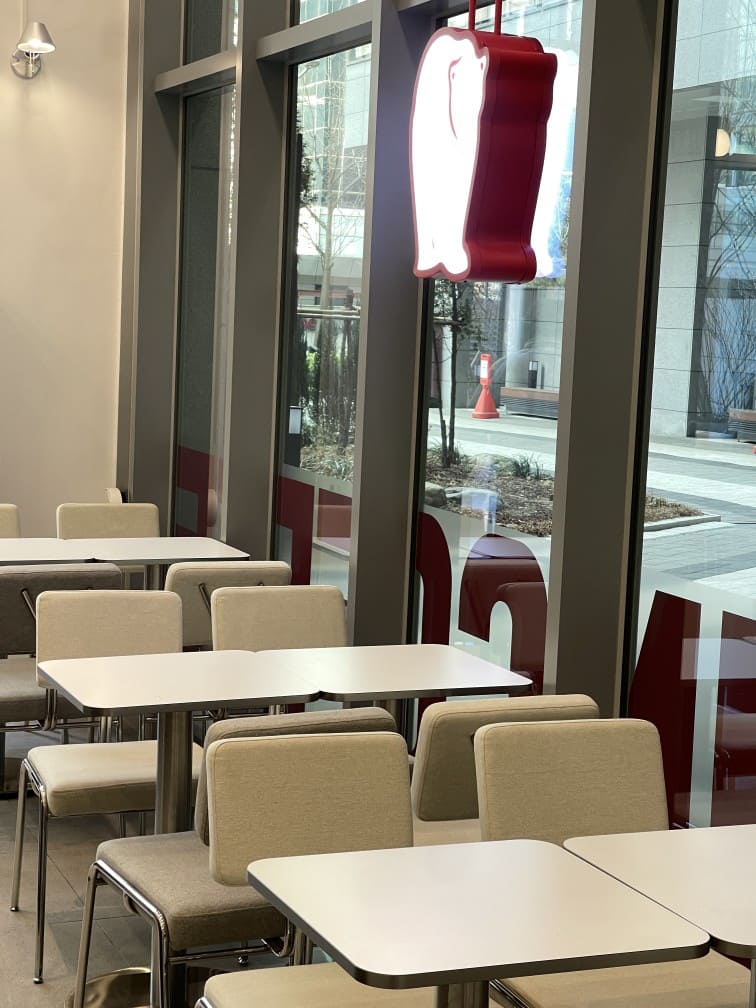 Bruin Coffee 카페 창가 좌석 에이맷 스튜디오 인테리어 시공 사례, 화이트 원형 테이블과 그레이 체어 배치의 자연광 다이닝 공간